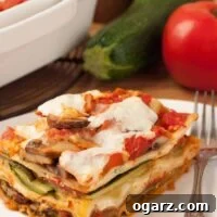 A serving of vegetable lasagna, layered zucchini, eggplant, mushrooms, and cheese, on a plate with a fork, a zucchini, tomato, and casserole of lasagna in the background.
