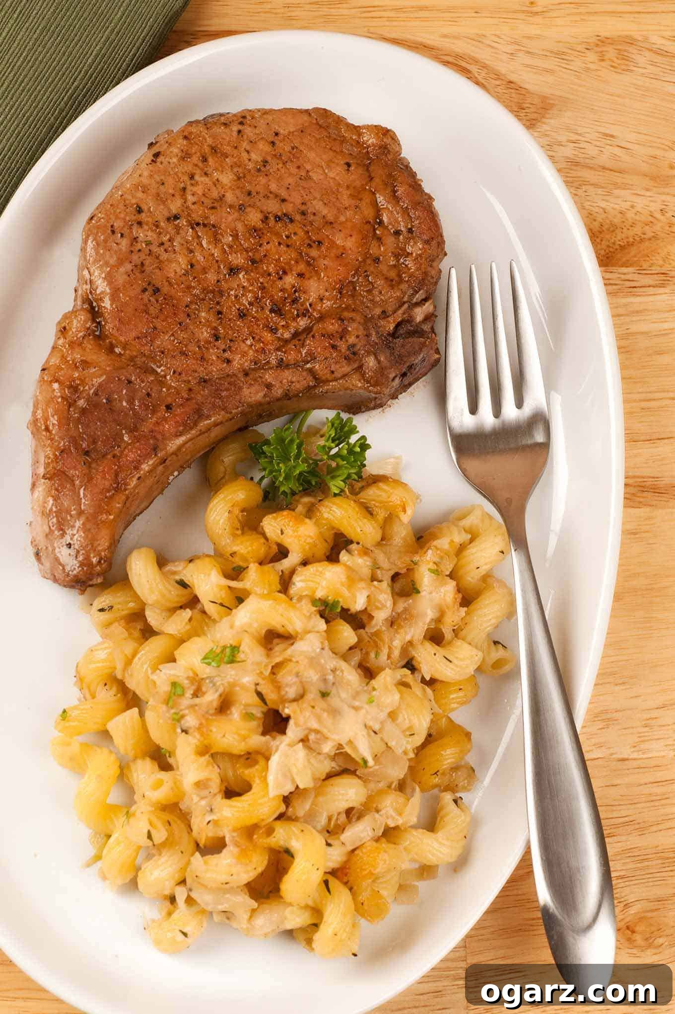 Caramelized Pork Rib Chops 2 A perfectly pan-seared bone-in pork rib chop with a golden crust, served on a white plate alongside cheesy cavatappi pasta and garnished with fresh parsley.