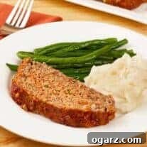 A vibrant close-up of a meatloaf slice on a plate, garnished with fresh herbs, alongside fluffy mashed potatoes and crisp green beans.