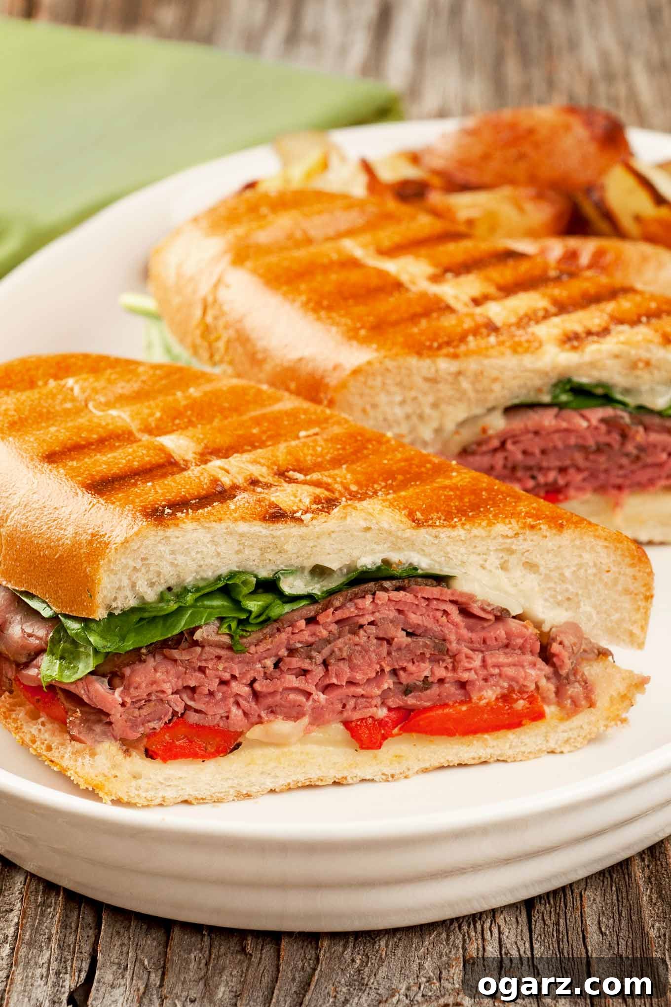 Savory Roast Beef Dual Cheese Panini 2 A plate with two halves of a toasted roast beef panini layered with rare deli roast beef, roasted red peppers, fresh spinach, melted fontina, and creamy blue cheese mayo.