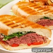 A plate with two halves of a toasted roast beef panini layered with rare deli roast beef, roasted red peppers, fresh spinach, melted fontina, and creamy blue cheese mayo.