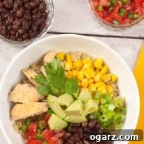 An overhead view of Southwest chicken quinoa bowl with black beans, corn, avocado, diced tomatoes, green onions, and fresh cilantro.