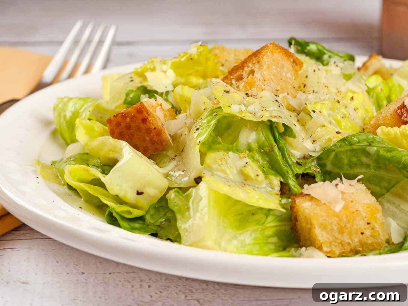 A close-up serving of a vibrant homemade Caesar salad, generously topped with golden brown, crispy garlic butter croutons and a dusting of freshly grated Parmesan cheese, showcasing its enticing textures and flavors.