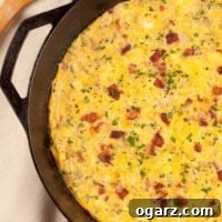 An overhead view of a bacon and cheese frittata in a cast iron pan garnished with extra bacon bits and chopped parsley.