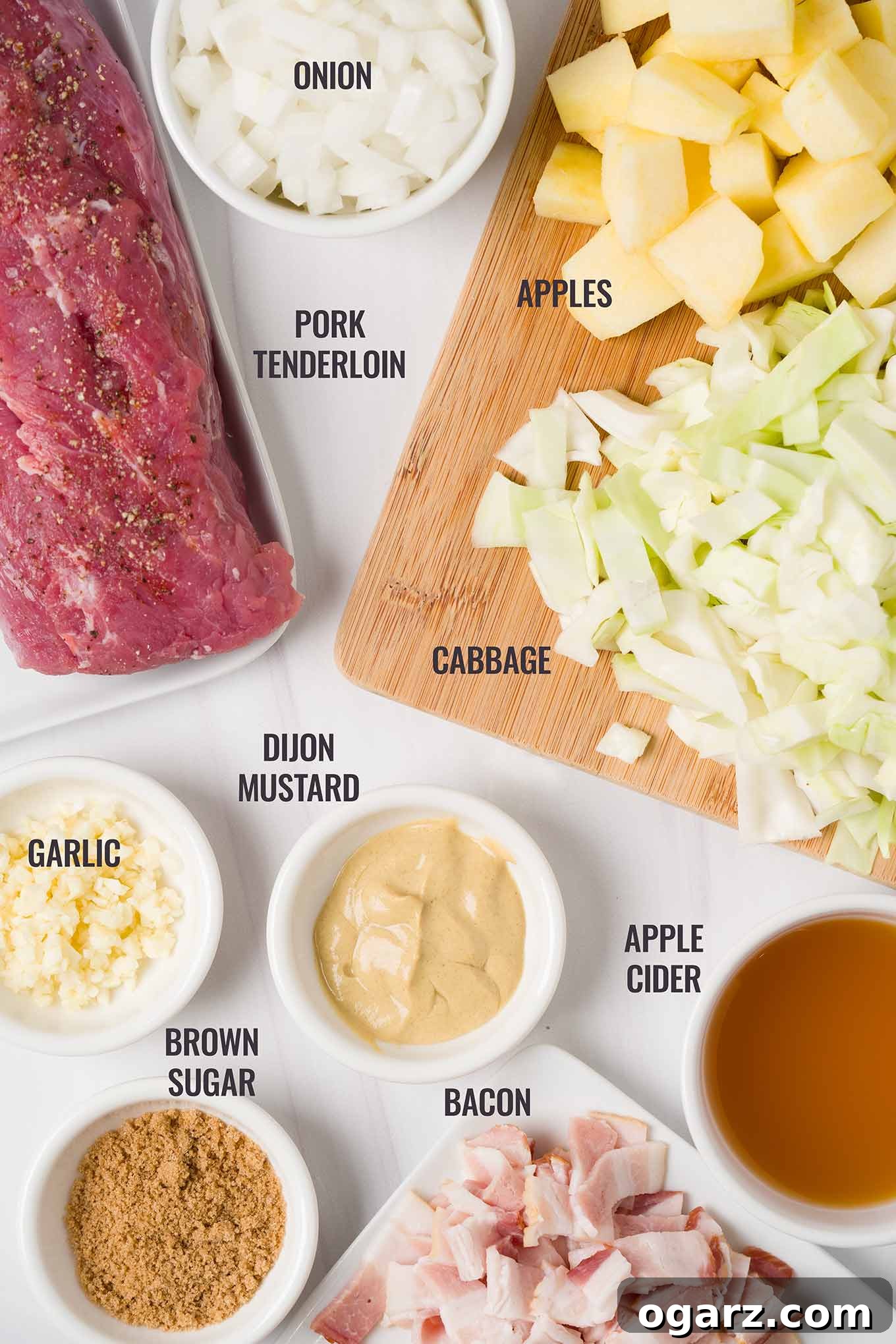 Apple and Cabbage Pork Tenderloin Braise 3 An overhead view of the fresh ingredients for braised pork tenderloin, including crisp apples, vibrant green cabbage, strips of bacon, brown sugar, Dijon mustard, and refreshing apple cider, all ready for preparation.