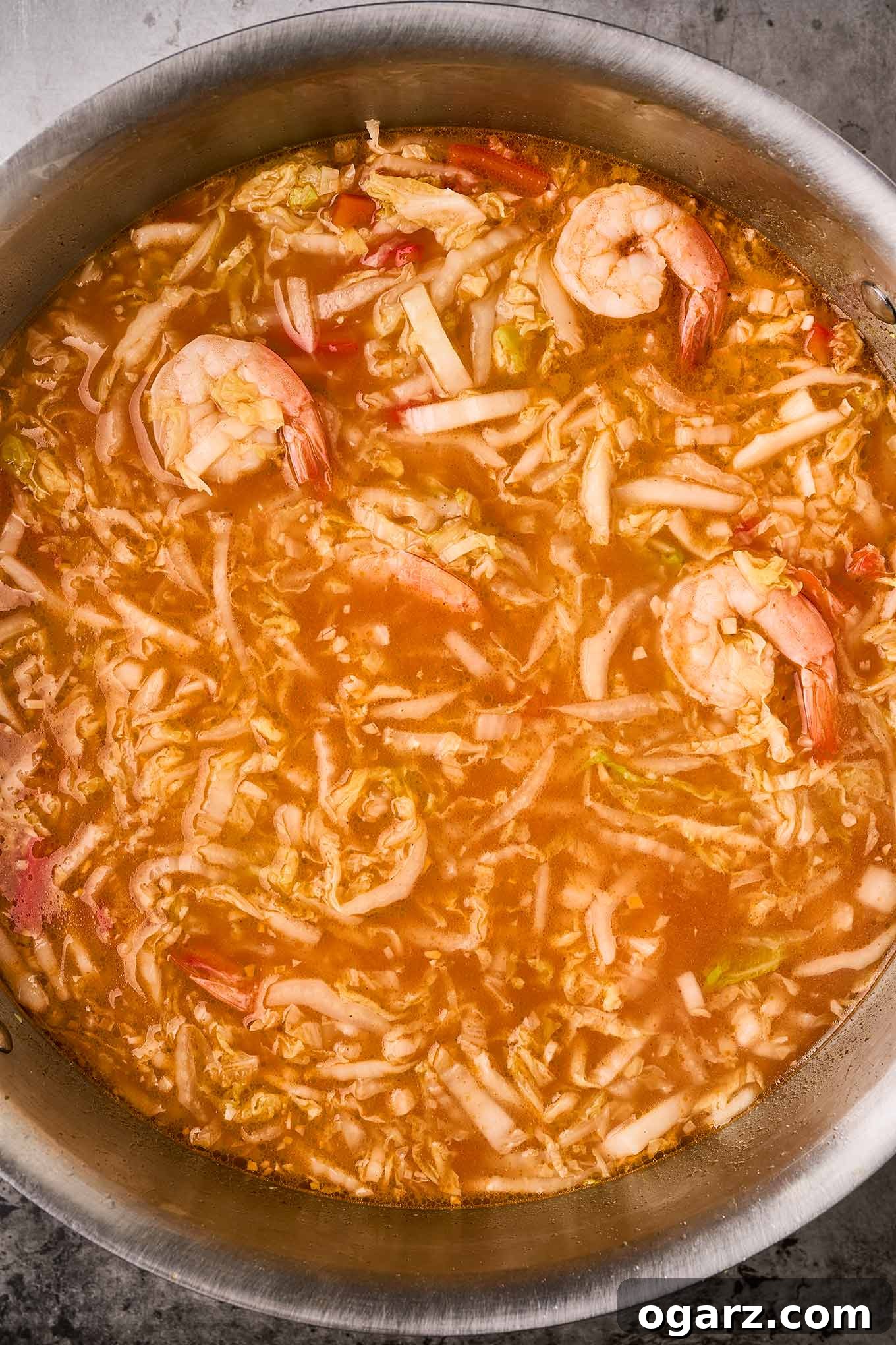 Fiery Shrimp Ramen Bowl 6 An overhead view of the vibrant, flavorful ramen broth mixed with crisp-tender Napa cabbage, red bell peppers, and succulent pink shrimp in a large soup pot, ready to be served into individual bowls.
