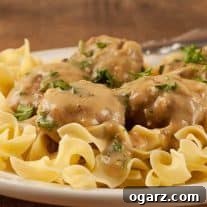 A close view of Swedish meatballs topped with chopped parsley and served over egg noodles, showing the creaminess of the sauce.