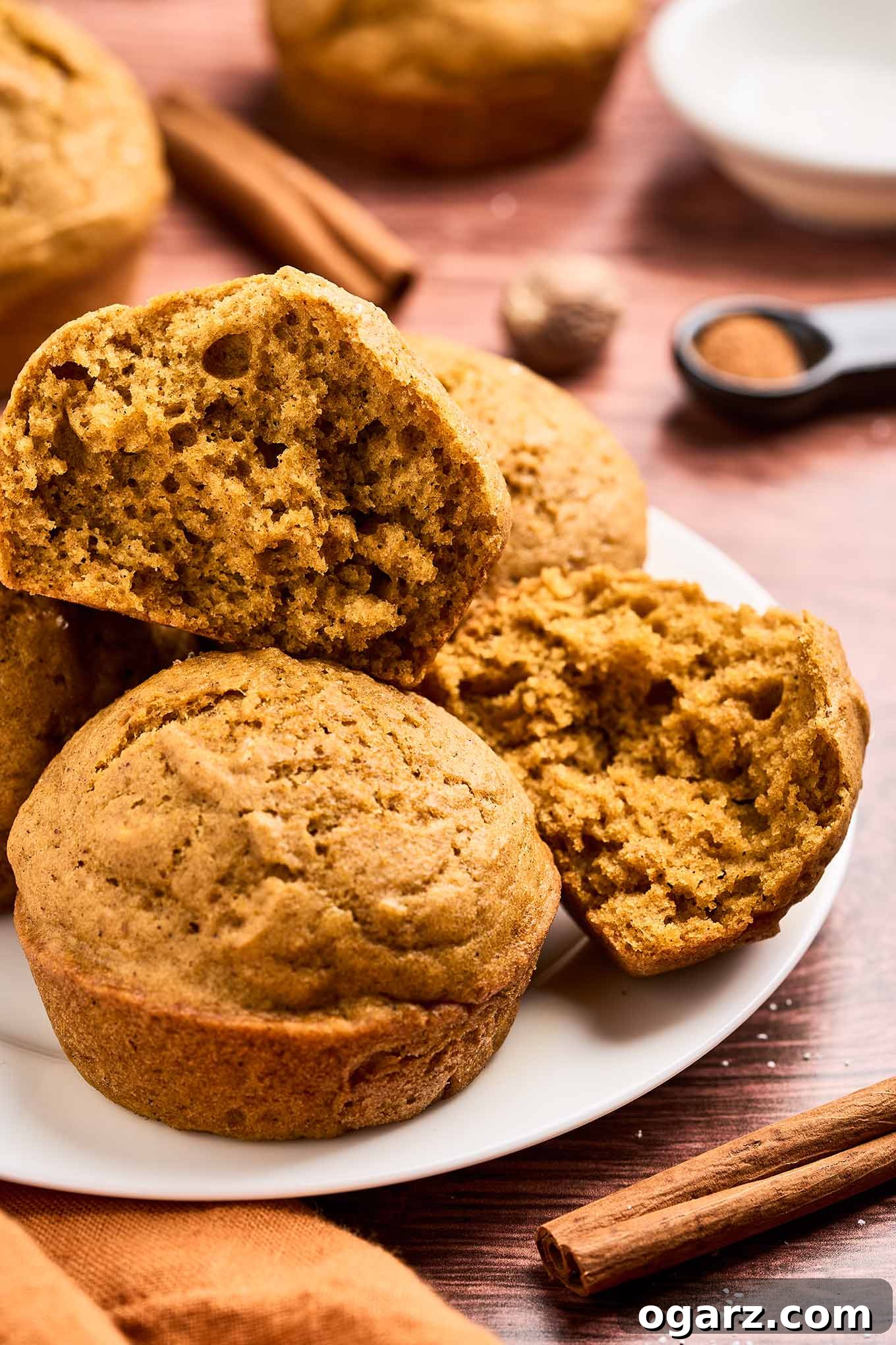 A plate of moist, airy pumpkin spice muffins with a golden-brown crust and soft, tender crumb on a plate surrounded by aromatic spices, showcasing their perfect texture.