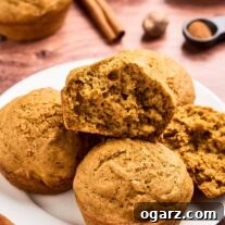 Close-up of moist and fluffy pumpkin spice muffins on a plate, one cut open to show soft texture, cinnamon sticks in the background.