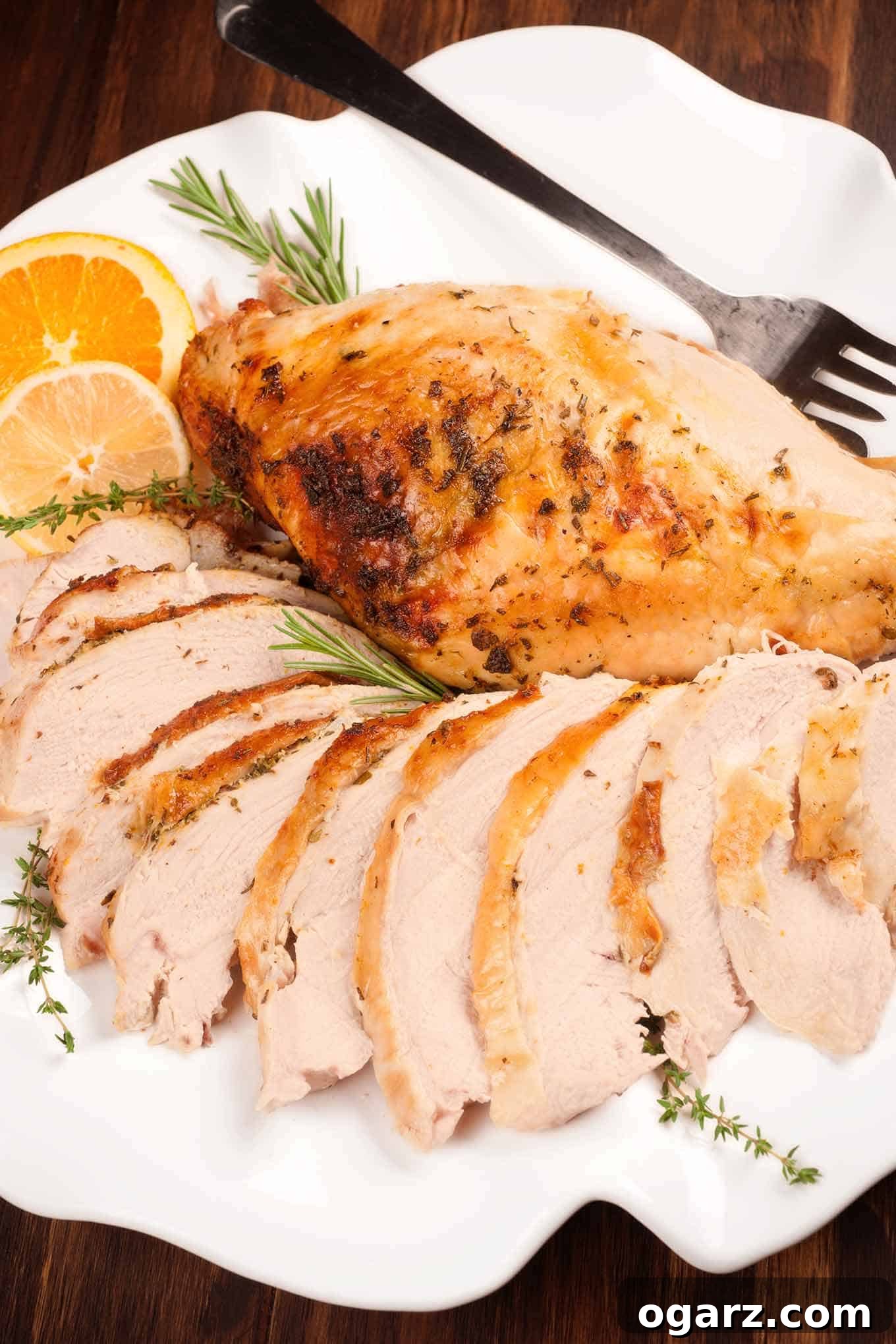 Zesty Herb Roasted Turkey Breast 2 Slices of perfectly roasted turkey breast with golden-brown skin on a platter, garnished with fresh herbs and citrus, alongside a whole uncarved turkey breast.