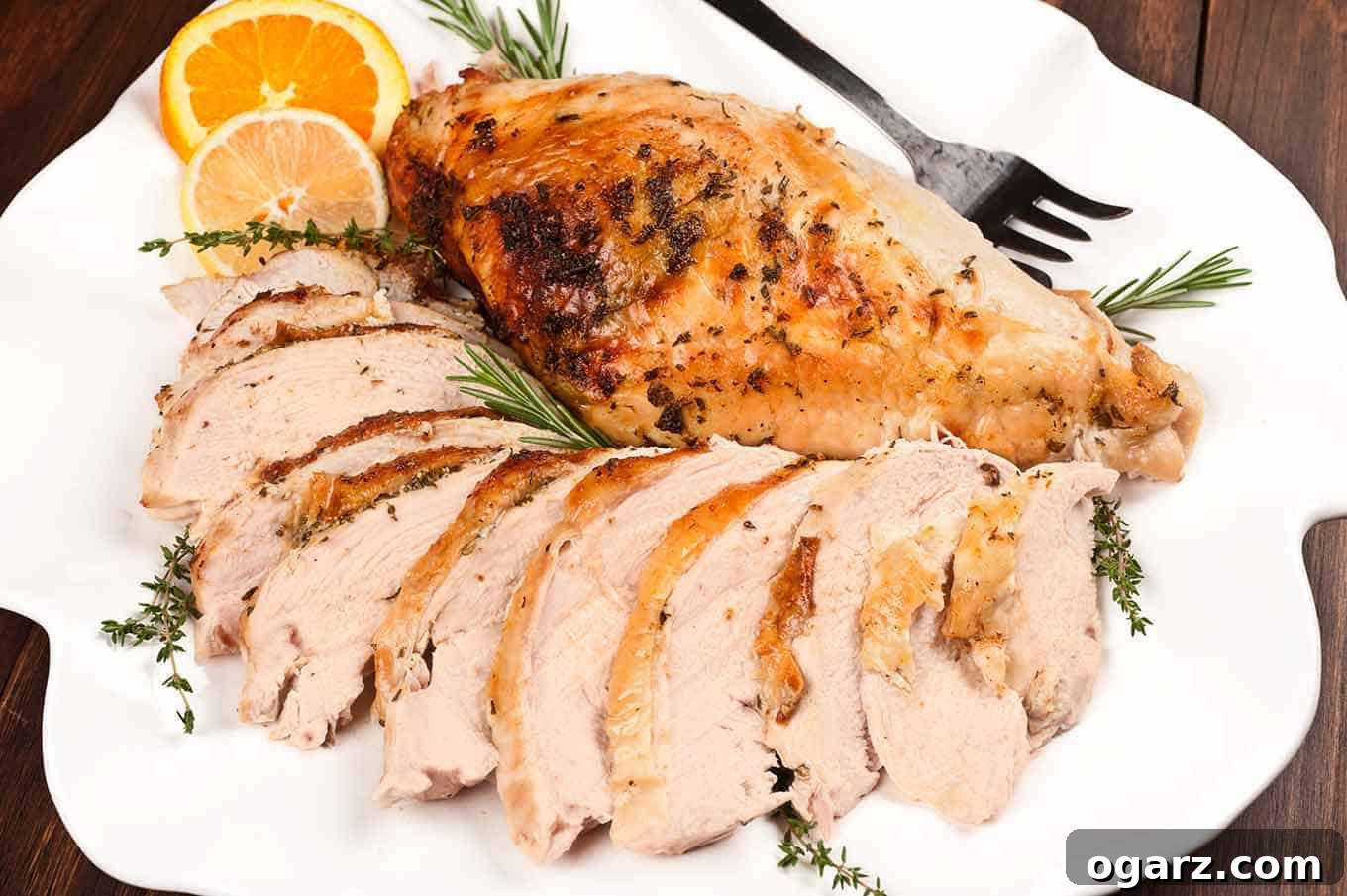 Zesty Herb Roasted Turkey Breast 4 A stunning platter showcasing a perfectly roasted citrus butter turkey breast with crisp, golden-brown skin. One half is elegantly carved into thick slices, while the other remains whole, garnished with fresh rosemary, thyme, and a serving fork.