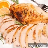 Partially carved roasted turkey breast with citrus butter on a serving platter, garnished with fresh herbs and oranges.
