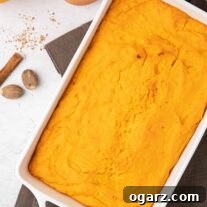 Baked casserole of fluffy whipped orange sweet potatoes with a fresh orange, cinnamon stick and nutmeg scattered on the side.