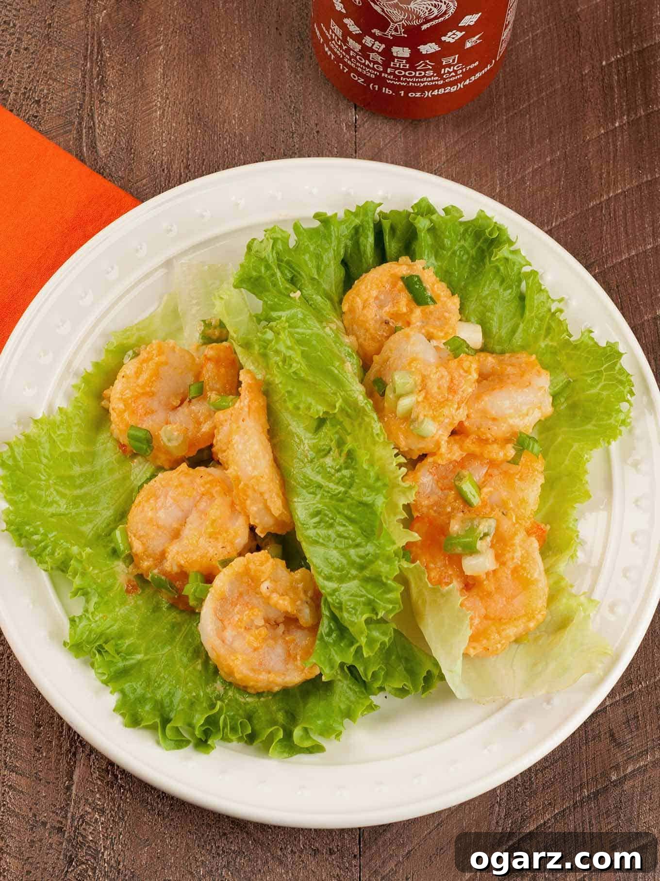 Bang Bang shrimp lettuce wraps served on a white plate, featuring crispy shrimp in spicy sauce wrapped in fresh green leaf lettuce, garnished with chopped green onions.