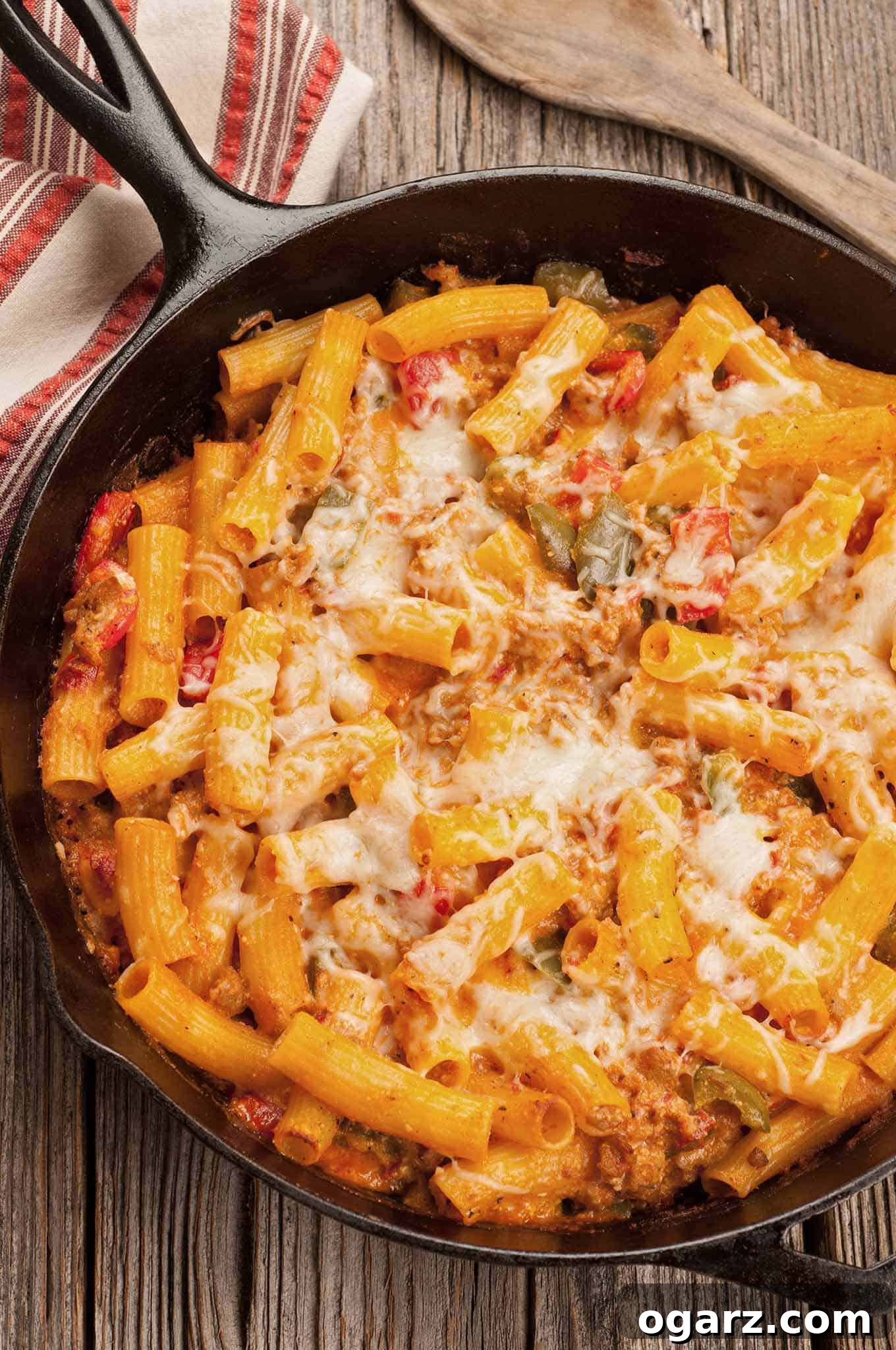 Hearty skillet baked ziti with Italian sausage and colorful bell peppers, topped with golden melted mozzarella, served in a rustic cast iron pan on a wooden table.