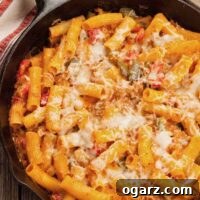 Close-up of skillet baked ziti with sausage and bell peppers, showing melted cheese and rich sauce, ready to be served.