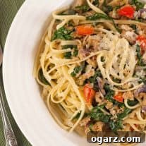 A bowl of linguine pasta tossed with crumbled sausage, wilted spinach, red bell peppers, and shredded Parmesan cheese.
