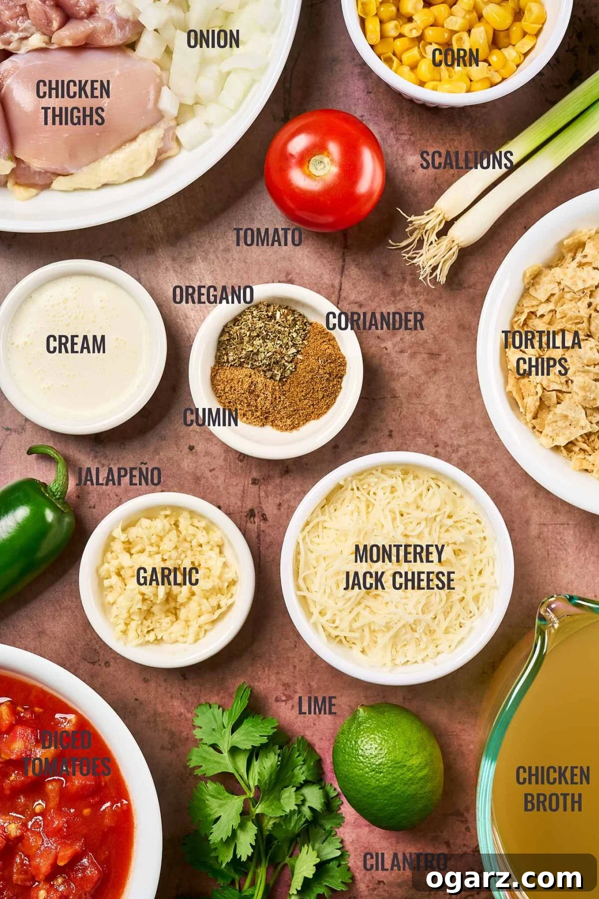 Velvety Chicken Tortilla Soup 3 A labeled, overhead view of the ingredients for creamy chicken tortilla soup including chicken thighs, tortilla chips, cheese, tomatoes, corn, jalapeno, lime, and cilantro, neatly arranged for preparation.