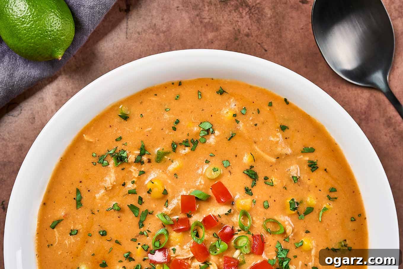 Velvety Chicken Tortilla Soup 5 A closeup view of a bowl of tortilla soup showing the garnish of chopped cilantro, sliced scallions, corn kernels, and diced fresh tomato, emphasizing the fresh, vibrant toppings.