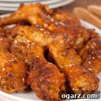 Close-up of golden, crispy oven-fried chicken wing drumettes with a glossy citrus-soy glaze and sesame seeds.