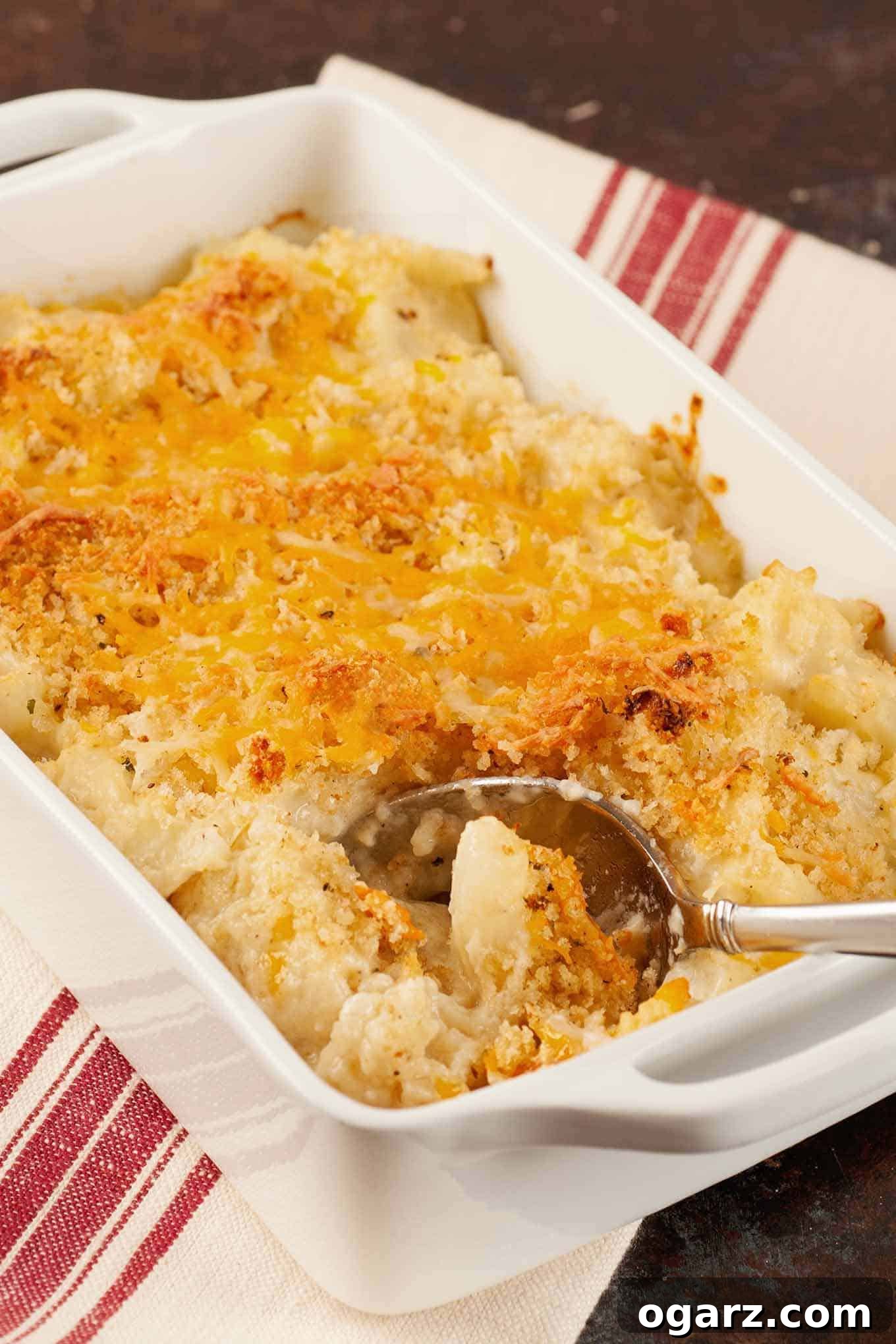 Golden Roasted Cauliflower Gratin 2 Golden brown roasted cauliflower gratin topped with melted cheddar cheese and crispy breadcrumbs in a white baking dish with a serving spoon, ready to be enjoyed.