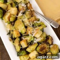 Warm Brussels sprouts Caesar salad with croutons and shaved Parmesan, served on a rectangular white platter.