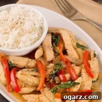 A close-up shot of a serving of Thai Basil Chicken, featuring tender chicken pieces, vibrant red bell peppers, and fresh green basil leaves, perfectly garnished and ready to eat.