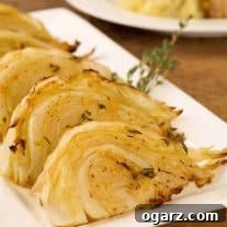 Wedges of herb and garlic roasted cabbage on a serving plate, garnished with thyme, dinner plate in the background.