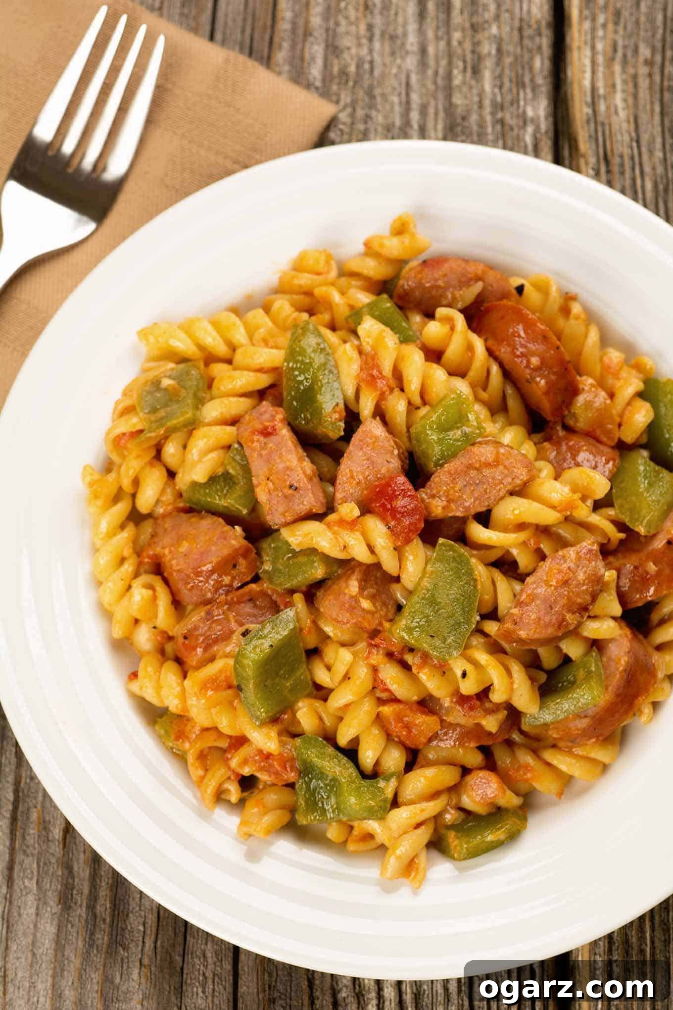 Smoky Sausage and Pepper Creamy Indulgence 2 Creamy pasta with smoked sausage and green bell peppers, served in a white bowl on a rustic wood surface.