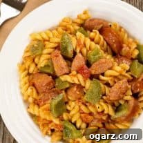Creamy pasta with smoked sausage and green bell peppers, served in a white bowl on a rustic wood surface.