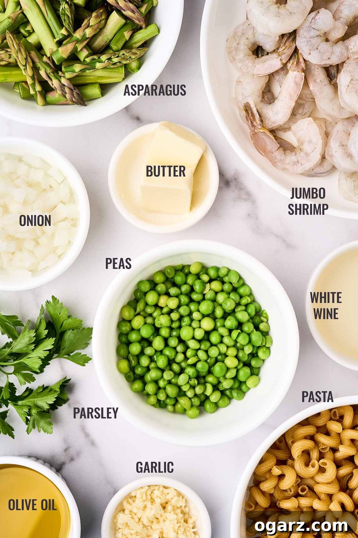 A labeled overhead view of the ingredients for shrimp pasta primavera; jumbo shrimp, asparagus, peas, pasta, white wine, and more.