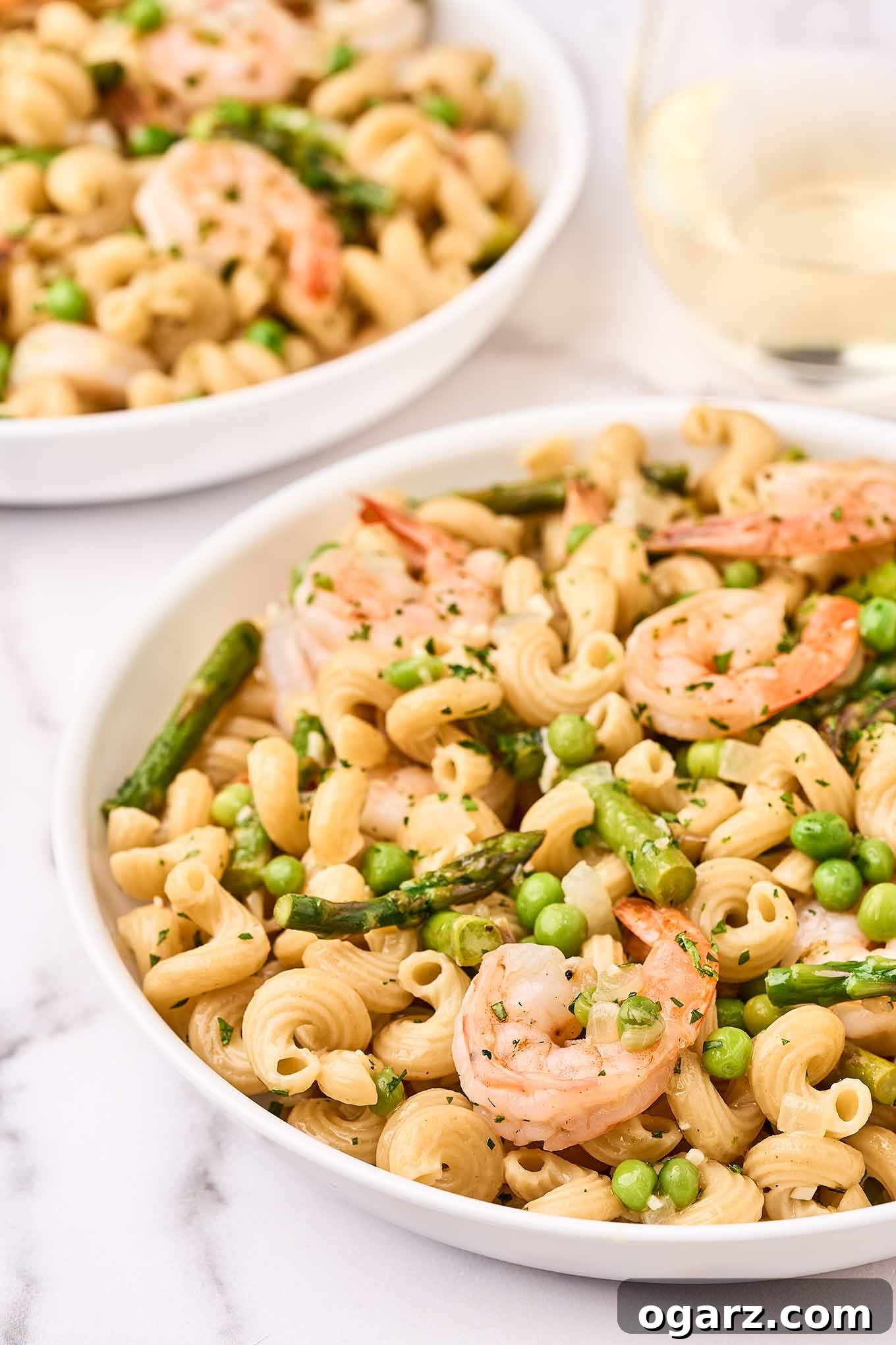 A close view of a bowl of pasta primavera with shrimp, another serving and a glass of wine to the rear.
