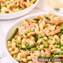 A close view of a bowl of pasta primavera with shrimp, another serving and a glass of wine to the rear.