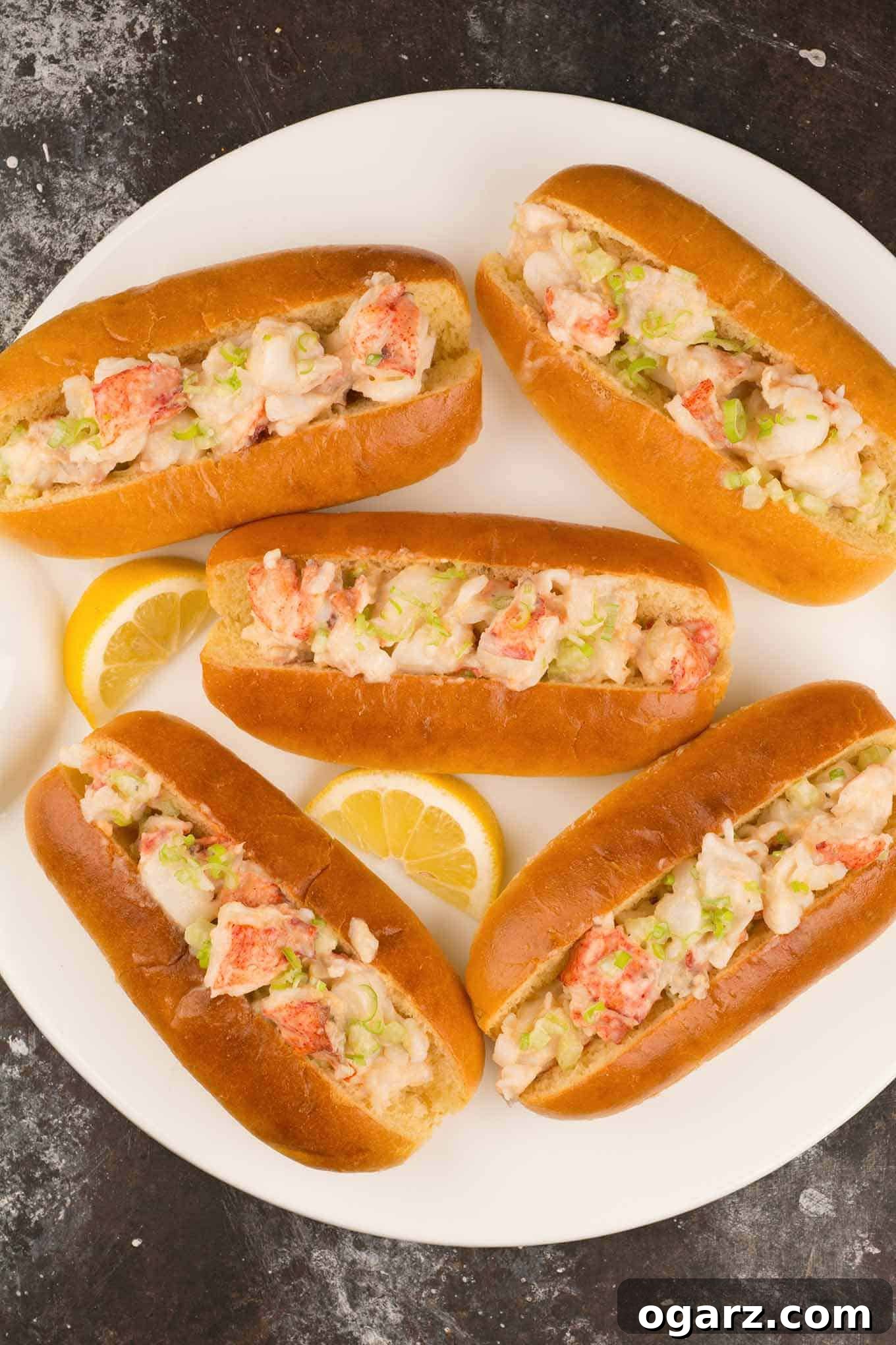 Seaside Perfection: New England Lobster Rolls 2 Five New England–style lobster rolls on a white plate, garnished with lemon slices.