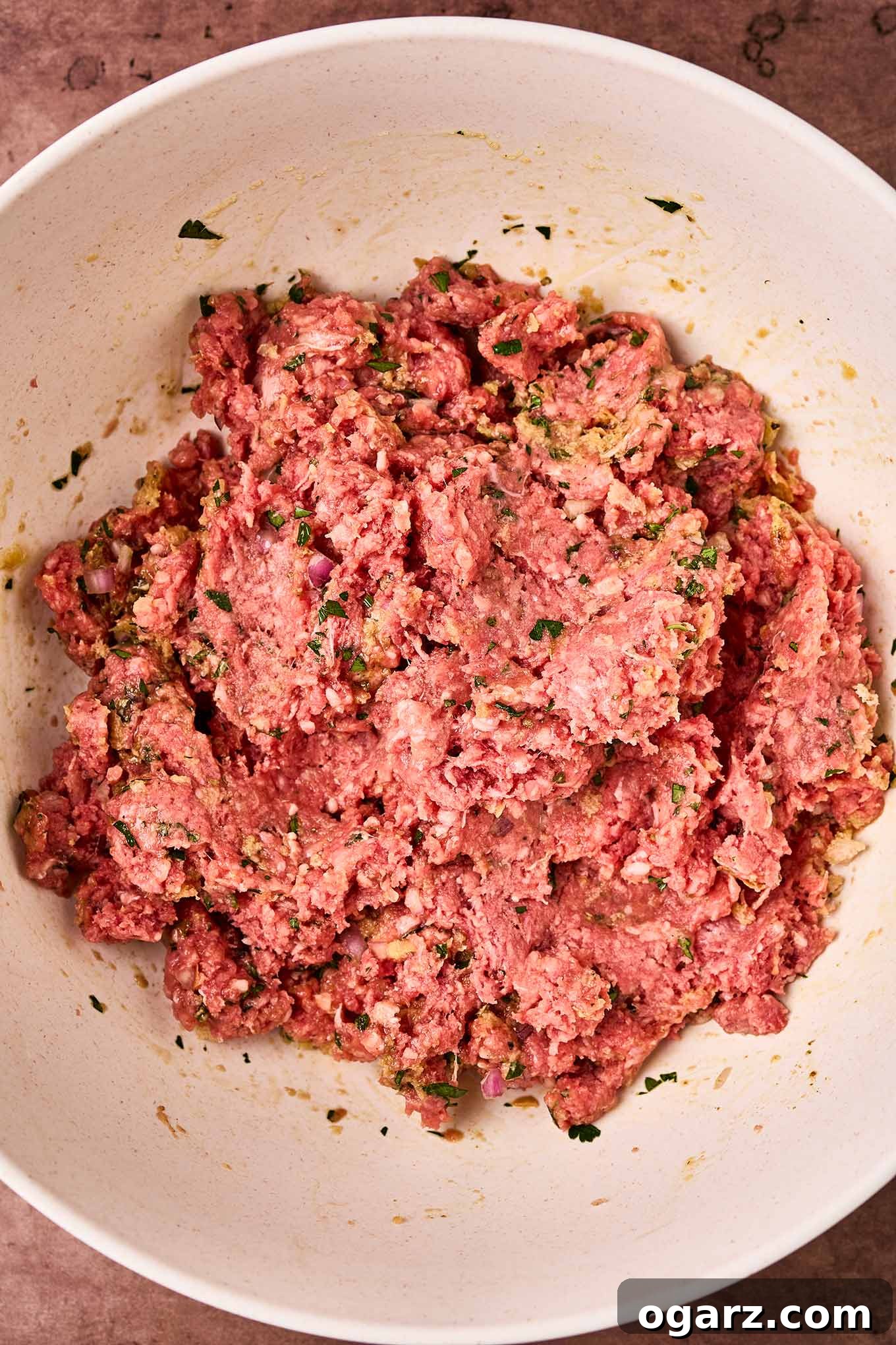 Soutzoukakia: Flavorful Greek Meatballs in Rich Tomato Sauce 6 A mixing bowl with Greek meatball meat mixture made with ground beef, egg, breadcrumbs, parsley, cumin, oregano, black pepper, and salt, ready to be rolled into meatballs.