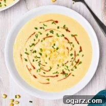 Velvety Sweet Corn Bisque 5 A light wooden background with two bowls of corn bisque surrounded by a black soup spoon, napkin, scattered corn, and chopped chives.