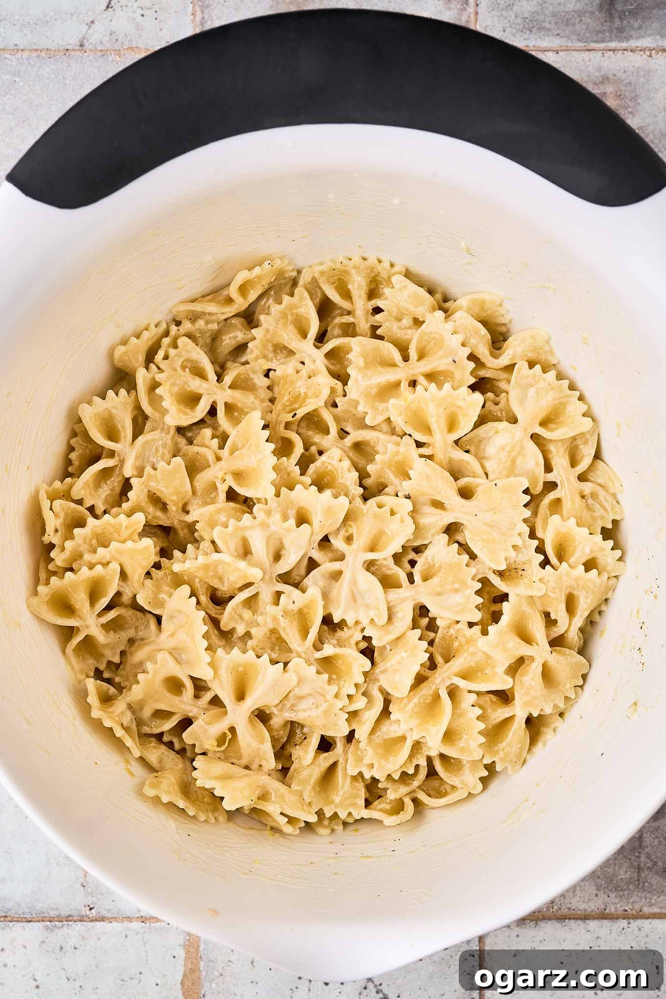 Zesty Lemon Cream Pasta Salad 5 A mixing bowl filled with farfalle dressed with creamy lemon dressing.