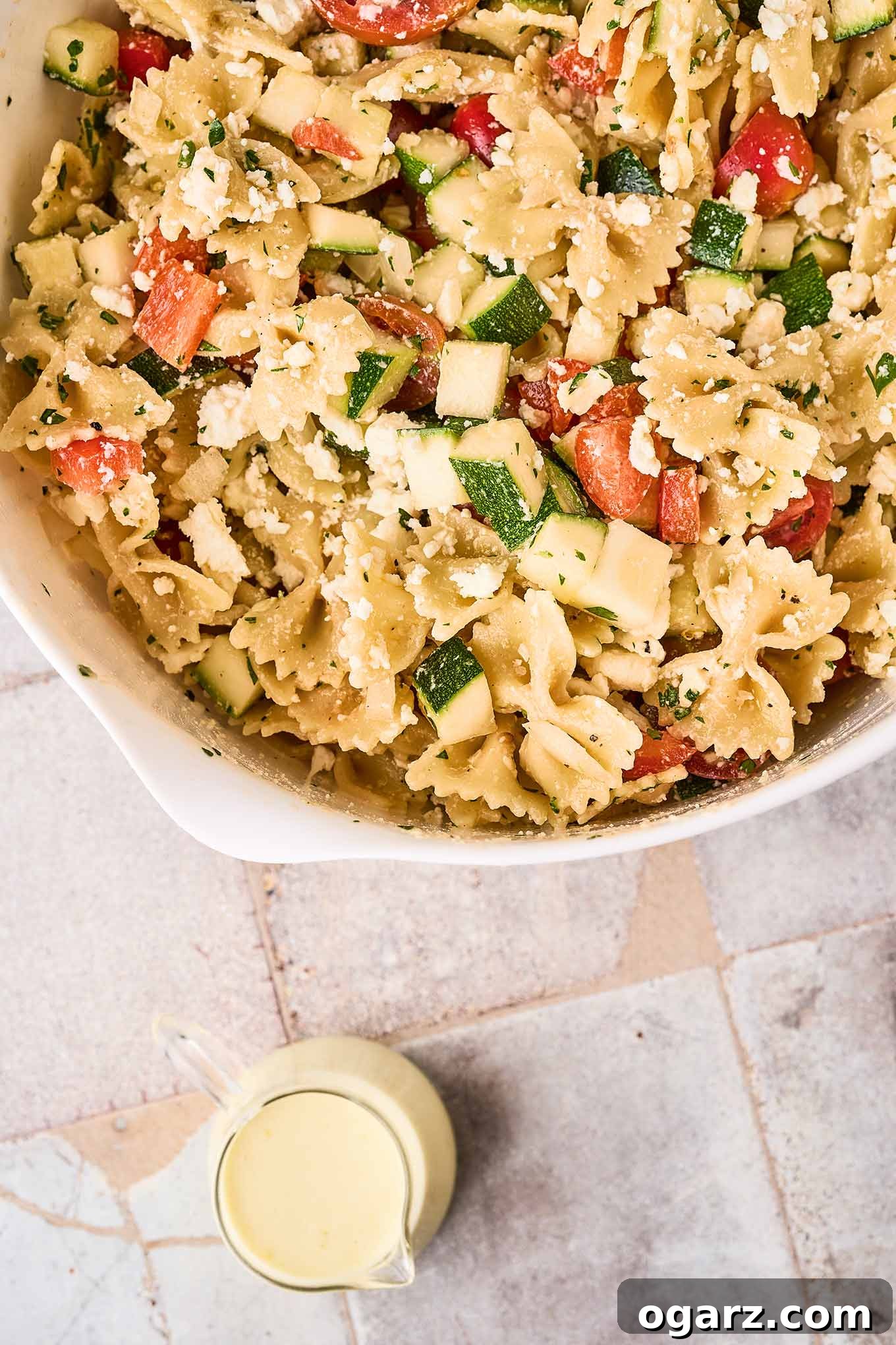 Zesty Lemon Cream Pasta Salad 6 Pasta, zucchini, tomatoes, red bell pepper, parsley, and feta cheese in a mixing bowl, ready to be combined with creamy lemon dressing.