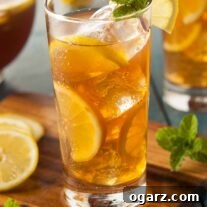 A chilled glass of bourbon-spiked iced tea, garnished with lemon and mint, with a pitcher in the background.