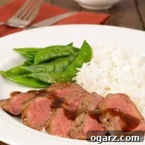 A plate of sliced, grilled flat iron steak drizzled with orange-hoisin sauce and served with steamed rice and snow peas, napkin and utensils in the background.