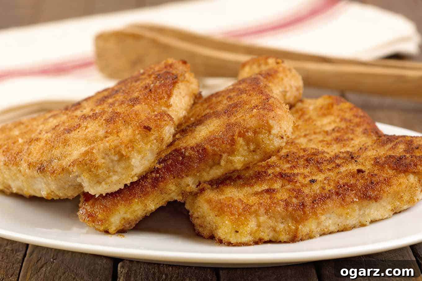 Golden brown, crispy breaded pork chops stacked on a serving plate with a pair of wooden serving tongs, ready to be enjoyed as a comforting meal.