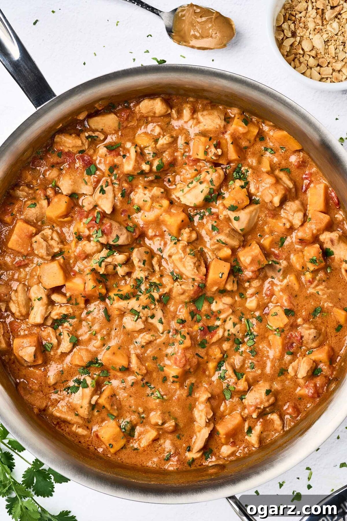 A sauté pan filled with African peanut stew with chunks of chicken thighs, sweet potato in a thick, savory, peanut butter and tomato based sauce.