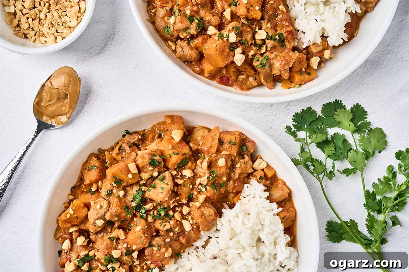 Two servings of West African chicken peanut stew and steamed white rice in bowls, garnished with chopped peanuts and cilantro, a dish with extra peanuts to the side.