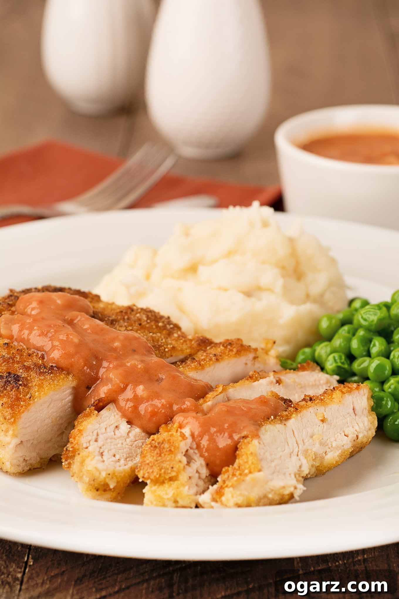 Crispy Pan-Fried Chicken with Tangy Tomato Gravy 2 Golden, crispy cornmeal-crusted chicken breasts with creamy Southern tomato gravy, served alongside fluffy mashed potatoes and vibrant green peas.