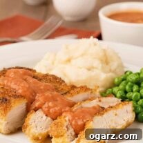 Pan-fried chicken with Southern tomato gravy served with mashed potatoes and green peas on a white plate.