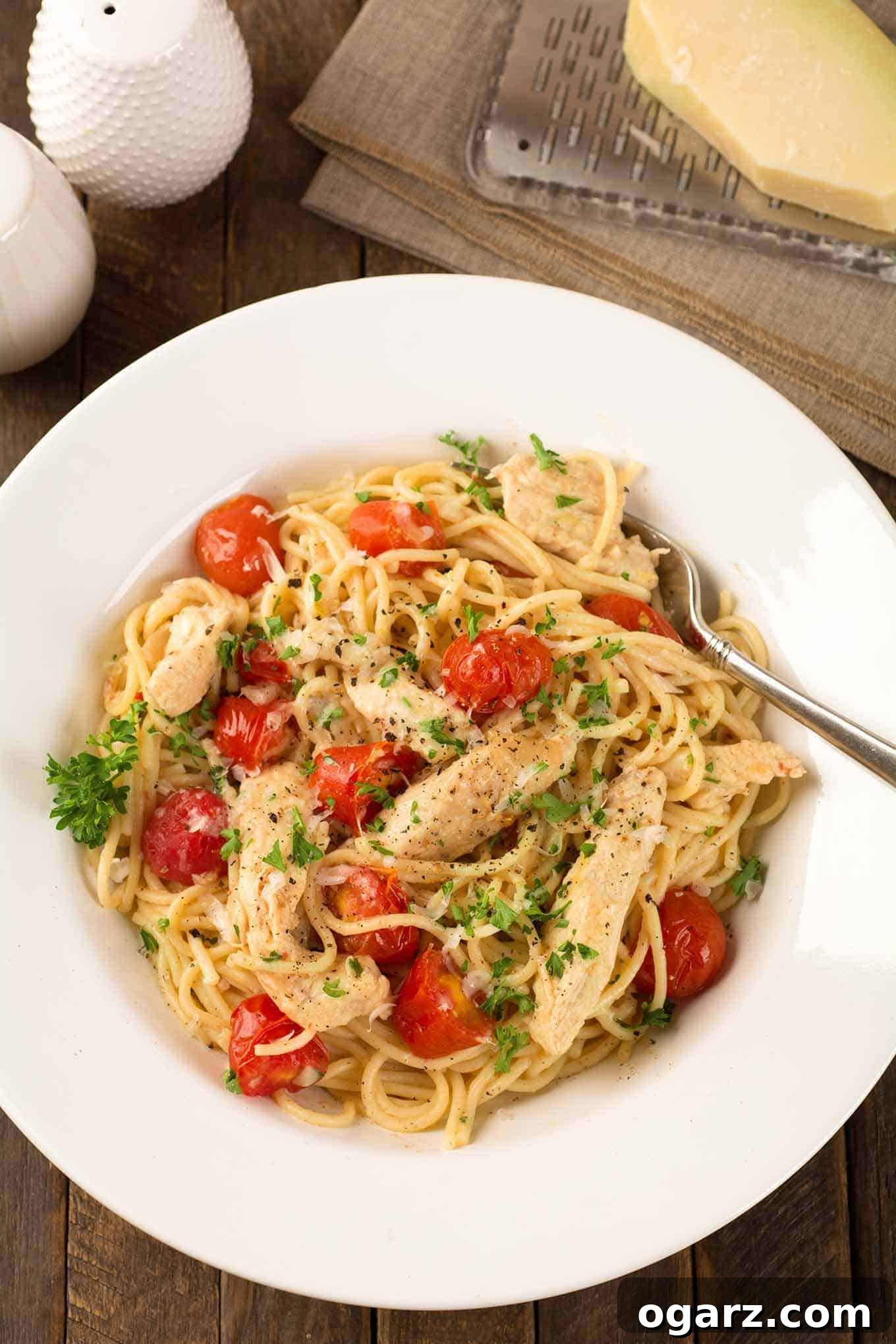 Zesty Lemon Chicken Pasta 2 A shallow bowl of spaghetti tossed with tender strips of boneless chicken, thin spaghetti, sweet grape tomatoes, and a fresh lemon and garlic pan sauce, parsley garnish on the top.
