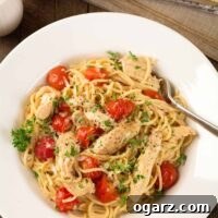 A shallow bowl of spaghetti tossed with tender strips of boneless chicken, thin spaghetti, sweet grape tomatoes, and a fresh lemon and garlic pan sauce, parsley garnish on the top.
