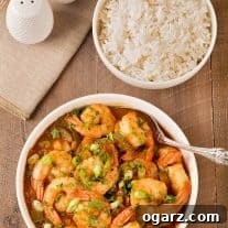 An overhead view of a bowl of Louisiana style shrimp stew in gravy with a bowl of steamed white rice and salt and pepper shakers to the rear and side.