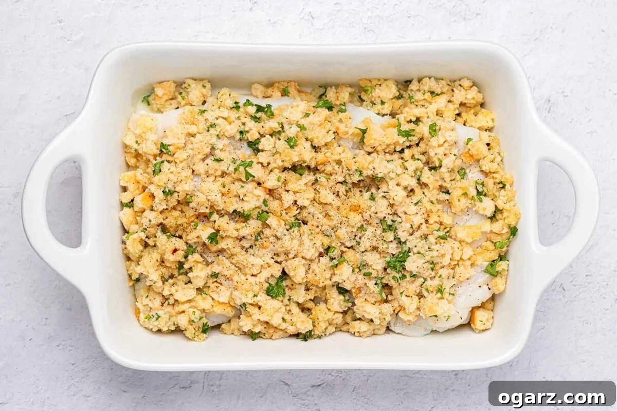 Crispy Crumb Cod Bake 6 A white, oblong baking dish filled with cod fillets and breadcrumb topping ready to be baked to golden perfection.