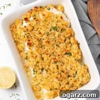 A casserole filled with baked cod fillets topped with breadcrumb stuffing, surrounded by linen napkin, wooden server, and lemon wedge. An inviting image of the final dish.
